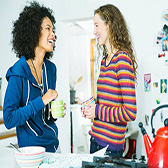 Two young women laughing in apartment kitchen. 