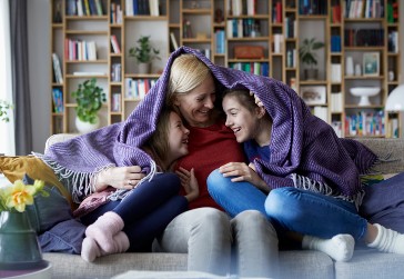 Mother and daughters huddled under a blanket and laughing. 