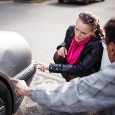 A man and woman inspect vehicle damage after an accident. 