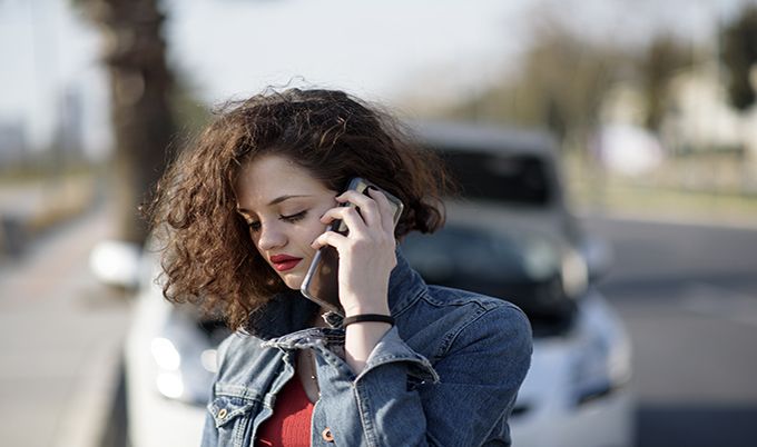 young woman on the phone in front of car.