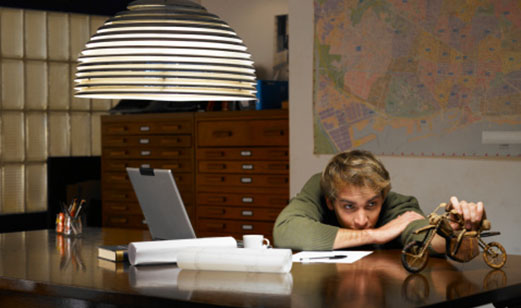 A young man sitting at a desk holding a model motorcycle while comparing motorcyle insurance on the computer.